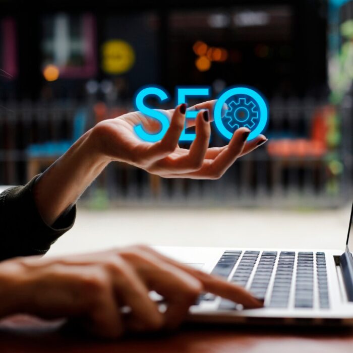 Hand holding blue neon SEO sign over a laptop.